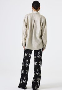 Beige, textuurgegeven, oversized overhemd met een kraag en knoopmanchetten, gecombineerd met zwarte fluwelen broek met zilveren en gouden abstracte bloemmotieven.