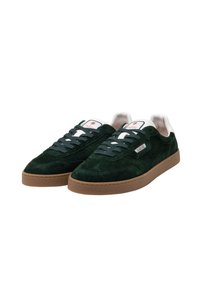 Grüne Wildledersneaker mit einem flachen Profil, ausgestattet mit einer Gummisohle, weißen Akzenten und flachen Schnürsenkeln. Branding auf der Zunge und der Seite.