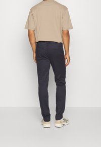 Męskie spodnie w luźnym kroju w kolorze granatowym, wykonane z gładkiego materiału, z dwiema tylnymi kieszeniami i płaskim przodem, połączone z beżowym t-shirtem z krótkim rękawem.