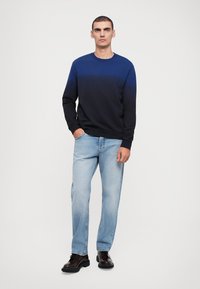 Sweatshirt em gradiente azul marinho com mangas longas, combinado com jeans claros. Modelo usa botas de couro escuras. Fundo simples.