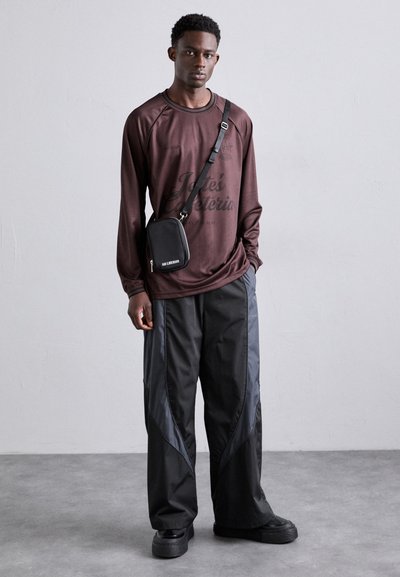 Long-sleeve maroon shirt with printed text, paired with black wide-leg pants featuring grey panel accents, and a small black crossbody bag.