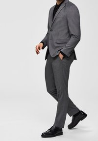 Gray tailored suit with a notch lapel, paired with a black dress shirt, slim-fit trousers, and black leather shoes. Smooth, textured fabric.