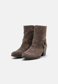 Botas de tobillo de ante marrón con una amplia correa y detalles de hebilla de metal, con un tacón apilado y diseño de punta redondeada.