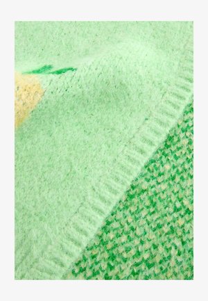 Puha, bolyhos anyagból készült zöld takaró, strukturált mintával. Különböző zöld árnyalatokat tartalmaz, sárga kiemeléssel és bordázott szegéllyel.