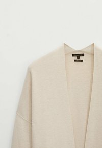 Vaahto-beige neulecardigan, jossa on avoin etuosa, leveät hihat ja pehmeä tekstuuri. Sisältää merkin ja hoito-ohjeet.