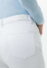 Jeans de algodón blancos con un diseño clásico de cinco bolsillos, bolsillos traseros con costuras sutiles y una etiqueta de marca en la cinturilla.
