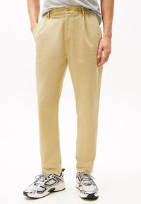 Chinos color caqui con un corte relajado, cinturilla elástica y bolsillos laterales. Combinados con zapatillas deportivas blancas y plateadas.
