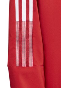 Rød atletisk stof med en struktureret mesh-panel og hvide lodrette striber, der fremhæver et sporty design.