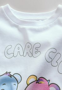 Weißes Baumwoll-T-Shirt mit der Aufschrift "CARE" in angesagten Bubble-Buchstaben und bunten Cartoon-Bär-Grafiken in Blau und Pink, ergänzt durch lila und gelbe Akzente.