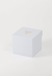 Une boîte carrée blanche avec une surface texturée, arborant un logo triangulaire doré dessus. Design fermé, minimaliste sans accents supplémentaires.