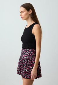 Schwarzes ärmelloses Top kombiniert mit einem ausgestellten Rock, der ein florales Muster in Pink, Weiß und Grün auf schwarzem Hintergrund zeigt.