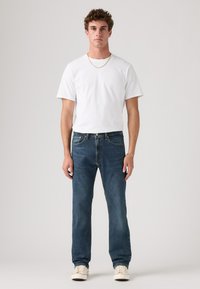 Witte T-shirt met korte mouwen, gecombineerd met donkerblauwe straight-leg jeans en witte sneakers, met een eenvoudig ontwerp en minimale hardware.