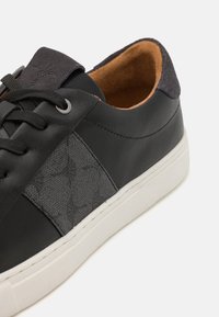 Svart skinnsneaker med teksturert sidepanel, grå semsket skinn detaljer, kontrasterende hvit såle og svarte snører. Brun innerlining synlig.