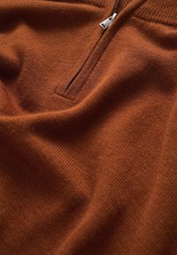 Brun stickad tröja med zip-krage, som har ett texturerat tyg och ribbade detaljer vid halslinningen. Slät, medelviktig material.
