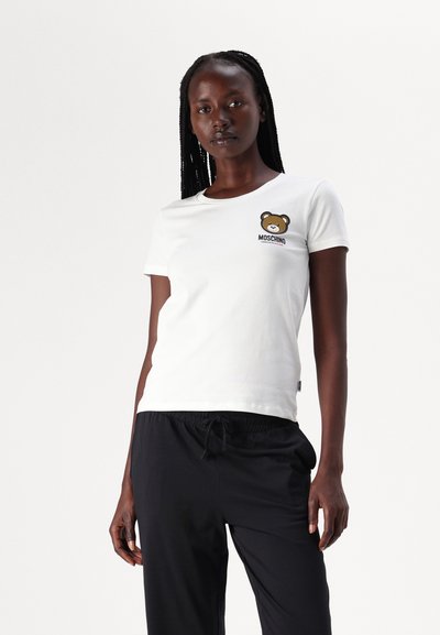 Hvid bomulds t-shirt med et bjørnegrafik og "Moschino" tekst på brystet. Korte ærmer og rund halsudskæring. Parret med sorte bukser.
