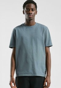 Korte mouwen katoenen t-shirt in gedempt blauw, met een ronde halslijn, rechte snit en kleine logopatch aan de onderrand. Vlotte textuur.