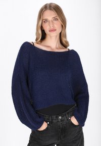 Granatowy krótki sweter o luźnym kroju, z teksturowanym wzorem i szerokimi rękawami, zestawiony z czarnymi, wysokimi dżinsami.