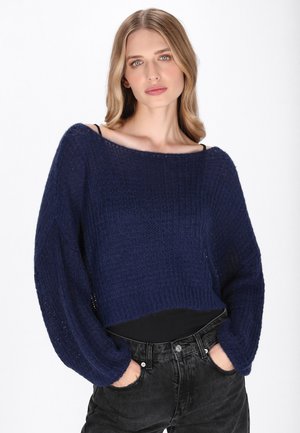 Granatowy krótki sweter o luźnym kroju, z teksturowanym wzorem i szerokimi rękawami, zestawiony z czarnymi, wysokimi dżinsami.