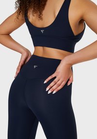 Set di reggiseno sportivo e leggings navy, realizzati in tessuto elasticizzato, con un design elegante caratterizzato da un accento logo e una texture liscia.