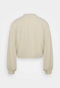Chaqueta corta de color crema con tejido de waffle texturizado, que presenta mangas largas y un cuello redondo, con un acabado suave y sin cierres.