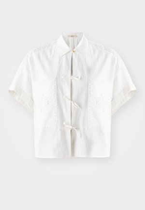 Camisa branca de manga curta com colarinho, apresentando detalhes bordados e laços decorativos à frente e nos bolsos. Tecido leve.