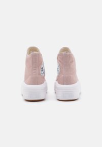 Vaaleanpunaiset kangaskorkeavartiset tennarit, joissa on valkoiset kumipohjat, ympyrän muotoinen logo ja näkyvät saumat.