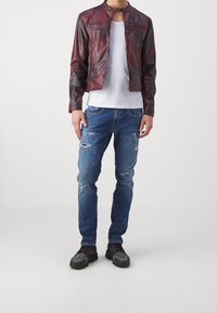Chaqueta de cuero burdeos para hombres con bolsillos con cremallera, combinada con jeans azules desgastados y zapatillas negras con detalles grises. Diseño de conjunto informal.
