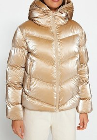 Giacca puffer metallizzata dorata con motivo a zigzag, chiusura con zip e cappuccio. Il tessuto ha una texture lucida ed è di design voluminoso.