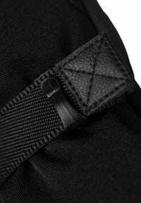 Nahaufnahme von schwarzem Stoff mit einem strukturierten Riemen, einer matten Kunststoffschnalle und einem dreieckigen Lederakzent.