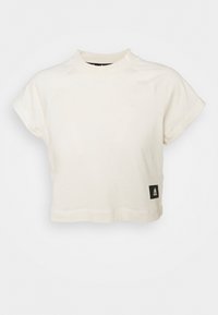 Oříznuté krémové tričko vyrobené z měkké látky, s krátkými rukávy, vysokým výstřihem a černou nášivkou loga Adidas na spodním lemu.