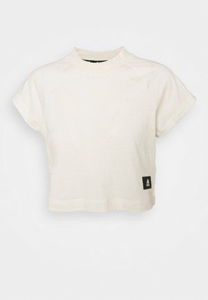T-shirt cropped de couleur crème en tissu doux, avec des manches courtes, un encolure haute, et une étiquette logo Adidas noire à l'ourlet.