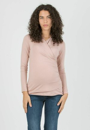 Long-sleeve wrap top in soft, light pink fabric with a draped front, paired with dark blue jeans. Smooth texture with a fitted style.
