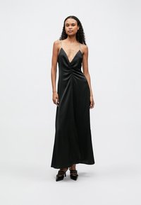 Rochie maxi din satin negru, cu gât adânc în V, detaliu frontal răsucit și bretele subțiri din argint. Textură netedă, design fluid, lungime până la glezne.