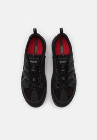 Chaussures de sport noires en maille et matériau synthétique, avec des accents rouges, un système de laçage intégré et une semelle intérieure rembourrée pour le confort.