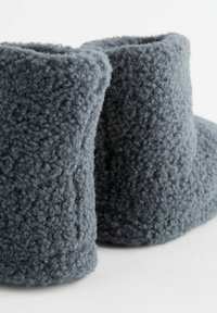 Graue, flauschige Knöchelstiefel mit einer weichen, strukturierten Oberfläche und abgerundetem Oberteil. Das Material wirkt plüschig und gemütlich, entworfen für Wärme und Komfort.