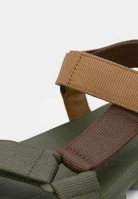 Πράσινο σανδάλι με φαρδιές λουρίδες από καφέ και ταμπά ύφασμα. Οι λουρίδες έχουν υφή και στερεώνονται με ραφές λεπτομέρειας.