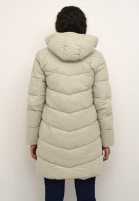 Beige, long puffer jacket with a hood, featuring chevron quilted design, smooth texture, and a slightly flared hem at the waist.