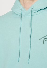 Sudadera azul claro hecha de suave tela de algodón. Cuenta con un bolsillo frontal, cordones y un sutil bordado del logo en el pecho.