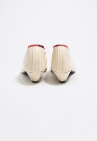 Zapatos de cuero beige con un acento rojo con estampado en la parte superior y un pequeño tacón negro. Textura suave con detalles de costura visibles.