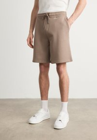 Brązowe bawełniane szorty z elastycznym pasem i sznurkiem. Posiadaj�ą boczne kieszenie i minimalistyczny design. W połączeniu z białymi sneakersami.