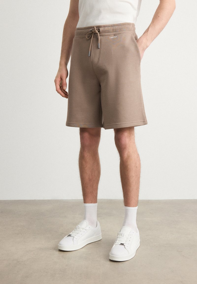 Brązowe bawełniane szorty z elastycznym pasem i sznurkiem. Posiadają boczne kieszenie i minimalistyczny design. W połączeniu z białymi sneakersami.