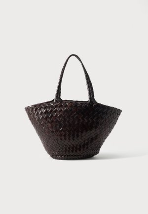 Geantă tote din piele împletită maro închis, cu două mânere și o formă trapezoidală largă, așezată pe o suprafață albă.