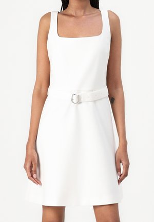 Vitt ärmlöst klänning med fyrkantig halsringning, åtsittande i midjan med ett vitt bälte och metallspänne, som har en utsvängd kjol.