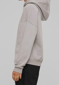 Lichtgrijze hoodie met een buidelzak, geribbelde manchetten en zoom, met een losse pasvorm en zachte textuur, gestyled met een capuchon.