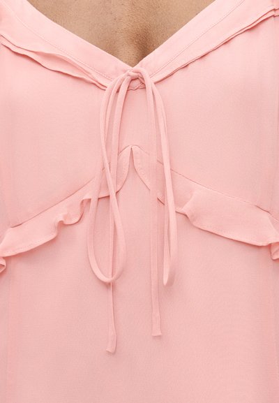 Ανοιχτόροζ μπλούζα με V-λαιμόκοψη, δεμένα κορδόνια μπροστά και λεπτές βολάν κατά μήκος της περιοχής του στήθους.