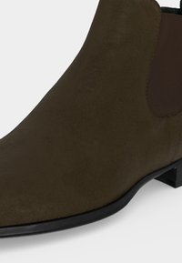 Bottine Chelsea en daim marron avec panneau latéral élastique et petit talon noir sur fond blanc.