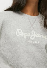 Sudadera gris claro con cuello acanalado, con bordado "Pepe Jeans" y "London" en blanco. Textura de tela de mezcla de algodón suave.