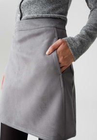 Gonna grigia in faux suede con una superficie liscia, dotata di tasca laterale e dettagli cuciti lungo i bordi. Design aderente.