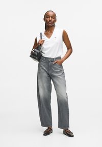 Top alb fără mâneci, cu decolteu în V, blugi gri deschis cu picioare largi, geantă neagră, pantofi plat negru cu catarame, texturi netede din bumbac și denim.