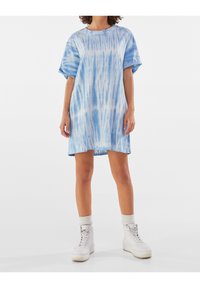 Modré tričko v šatičkovém stylu s tie-dye vzorem, volného střihu a krátkými rukávy, s horizontálním vzorem a délkou nad kolena, v kombinaci s bílými teniskami.